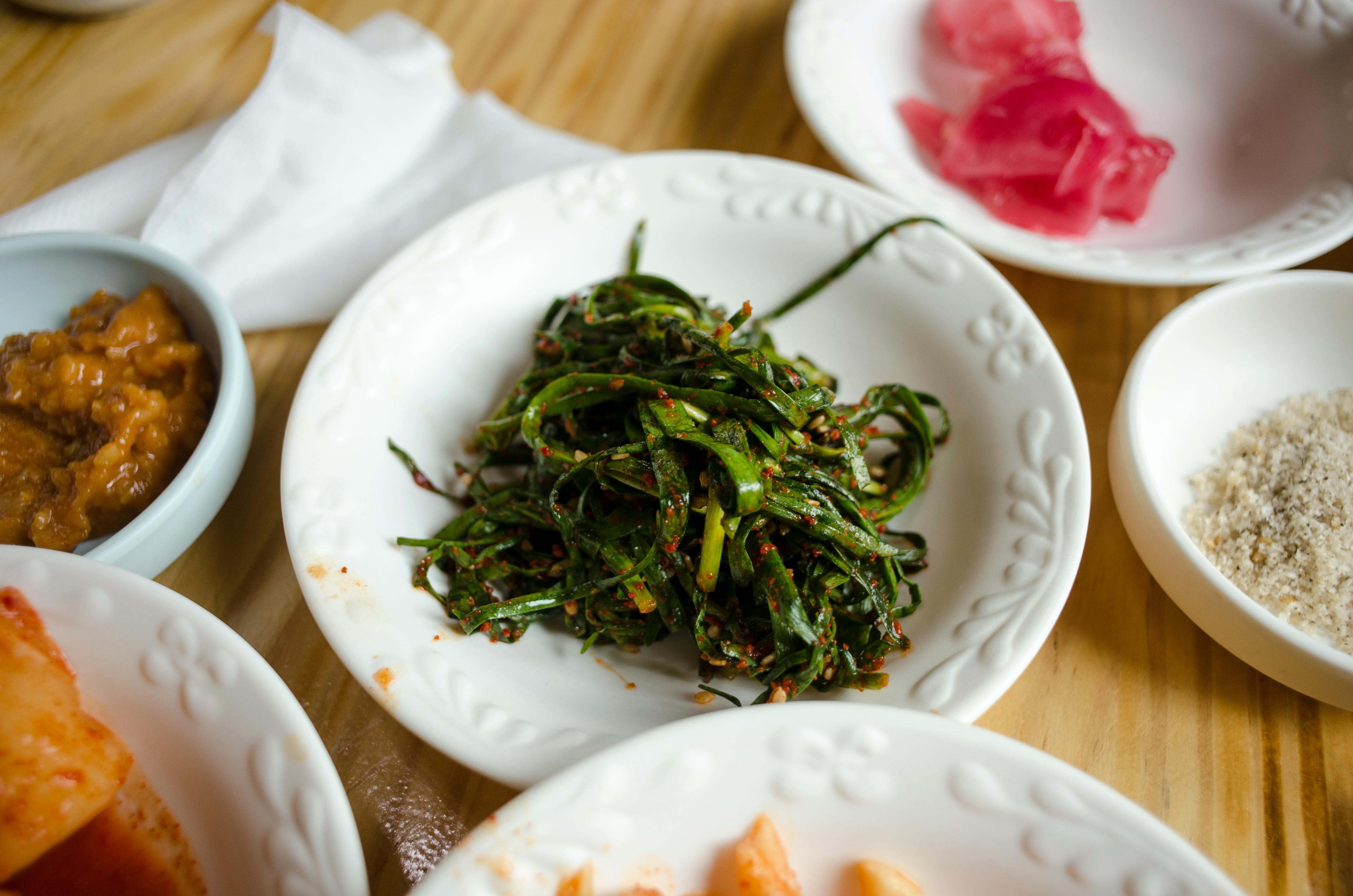 Close-up of assorted Korean side dishes including seasoned seaweed in white bowls on a wooden table.