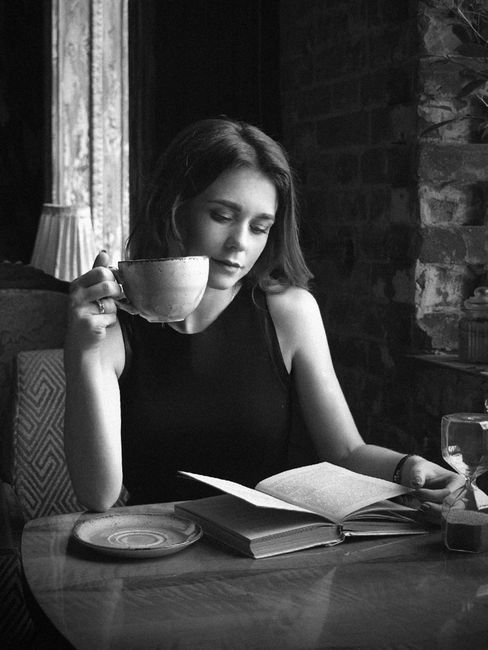 Black-and-white photo of a woman enjoying a book and coffee in a cozy, rustic cafe.