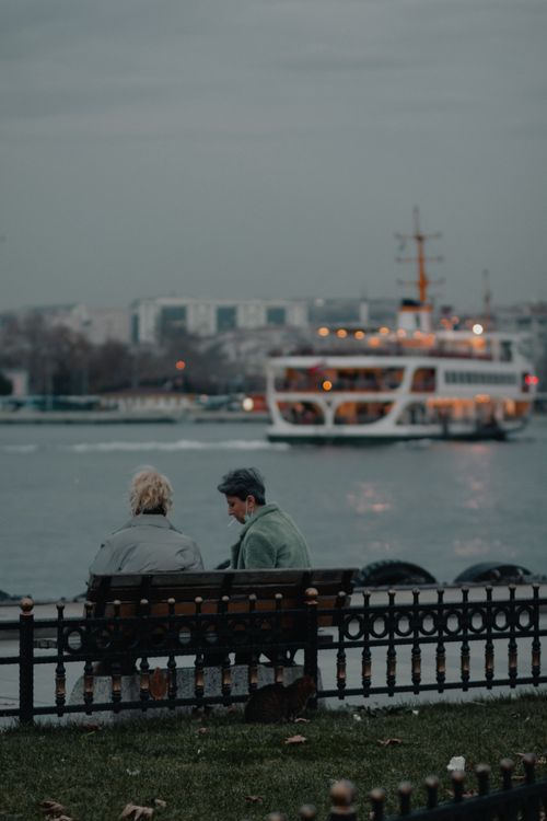 Free Two people sitting by the Bosphorus in Istanbul with a ferry in the background. Stock Photo