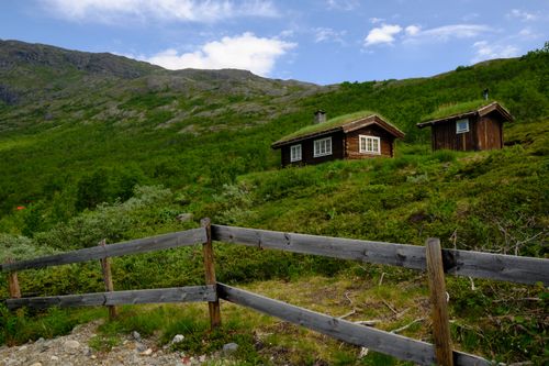 Free Scenic view of rustic wooden cabins on a lush green hill under a blue sky. Stock Photo