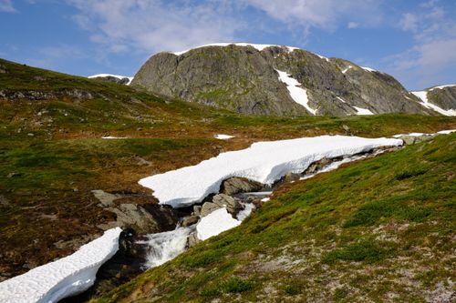 Free A serene landscape of snow-capped mountains and a flowing stream surrounded by lush greenery. Stock Photo