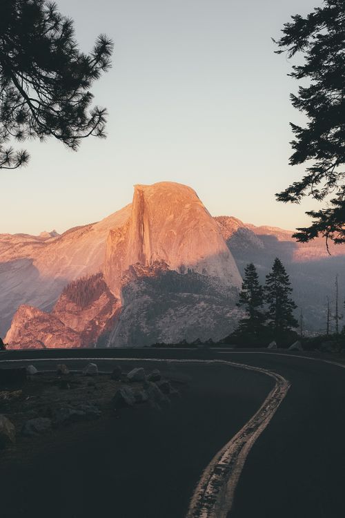 Free Enjoy a scenic view of the iconic Half Dome in Yosemite National Park surrounded by nature and a winding road. Stock Photo