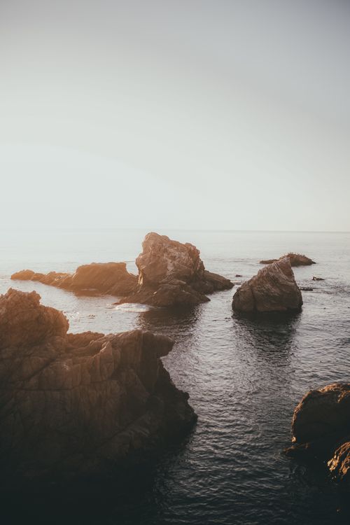 Free Peaceful view of rocky coastline with gentle waves at sunrise, ideal for serene nature imagery. Stock Photo