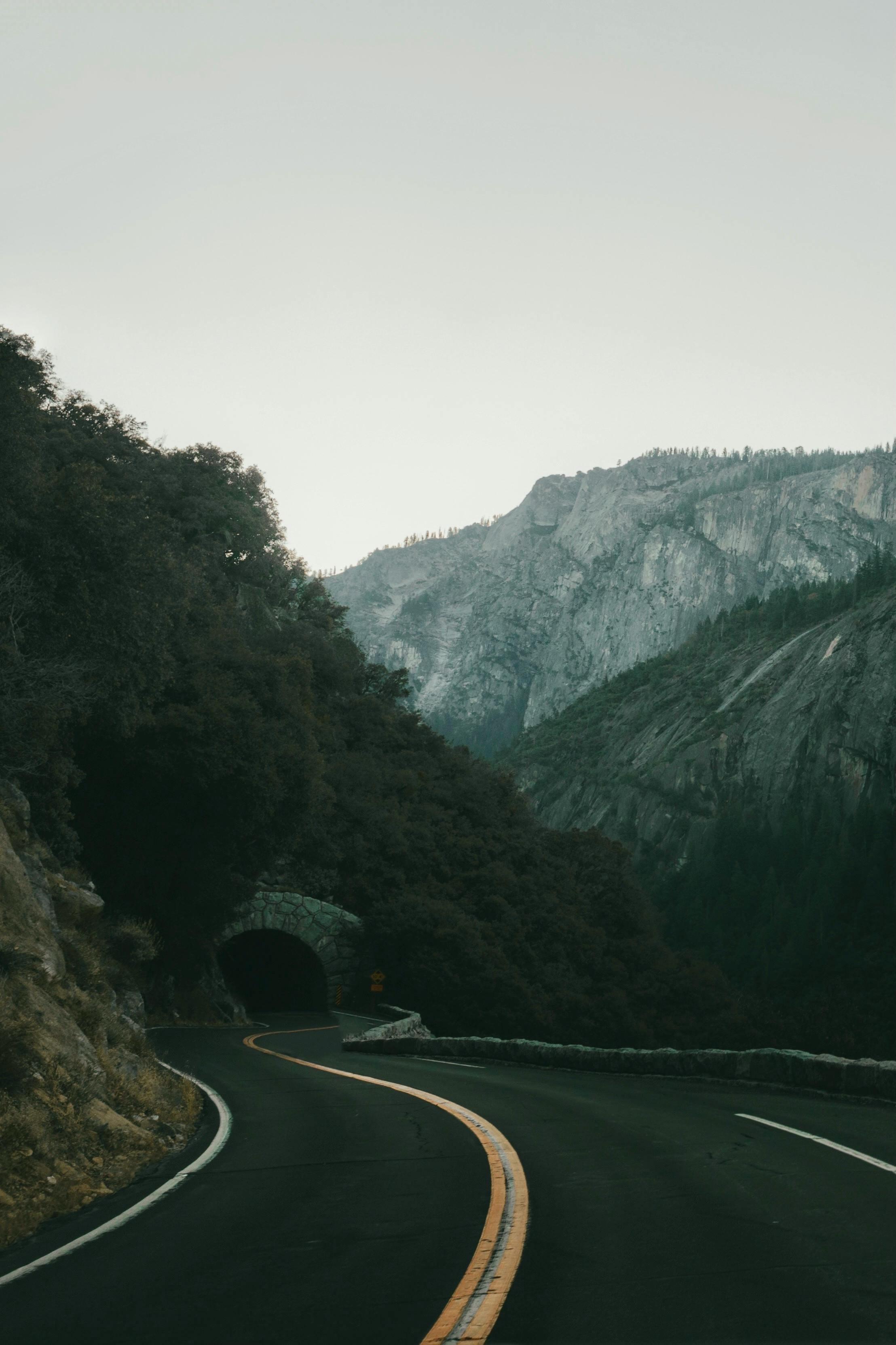 Curving mountain road disappearing into a tunnel with majestic rocky backdrop.