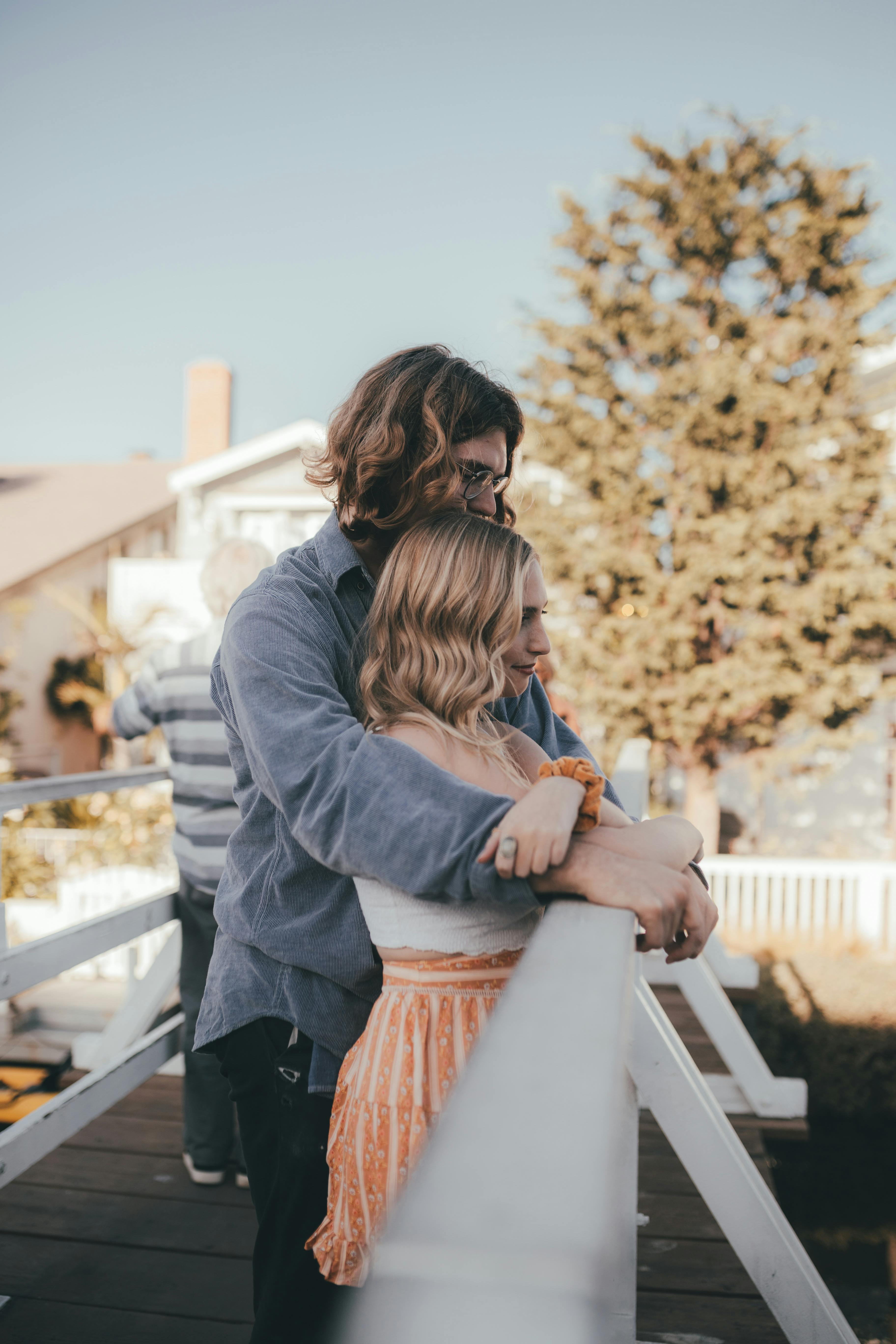 A couple embraces on a sunny bridge, captured in a serene outdoor setting.