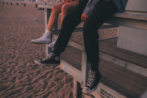 Free A couple sitting on a lifeguard stand at the beach wearing Converse sneakers during sunset. Stock Photo