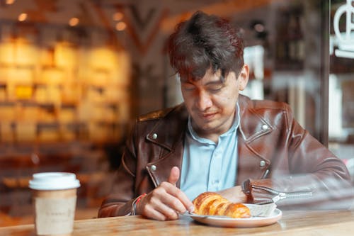 Photo of a Man in a Brown Leather Jacket Looking at a Croissant