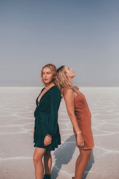 Two stylish women posing back to back in a desert setting, showcasing trendy outfits.