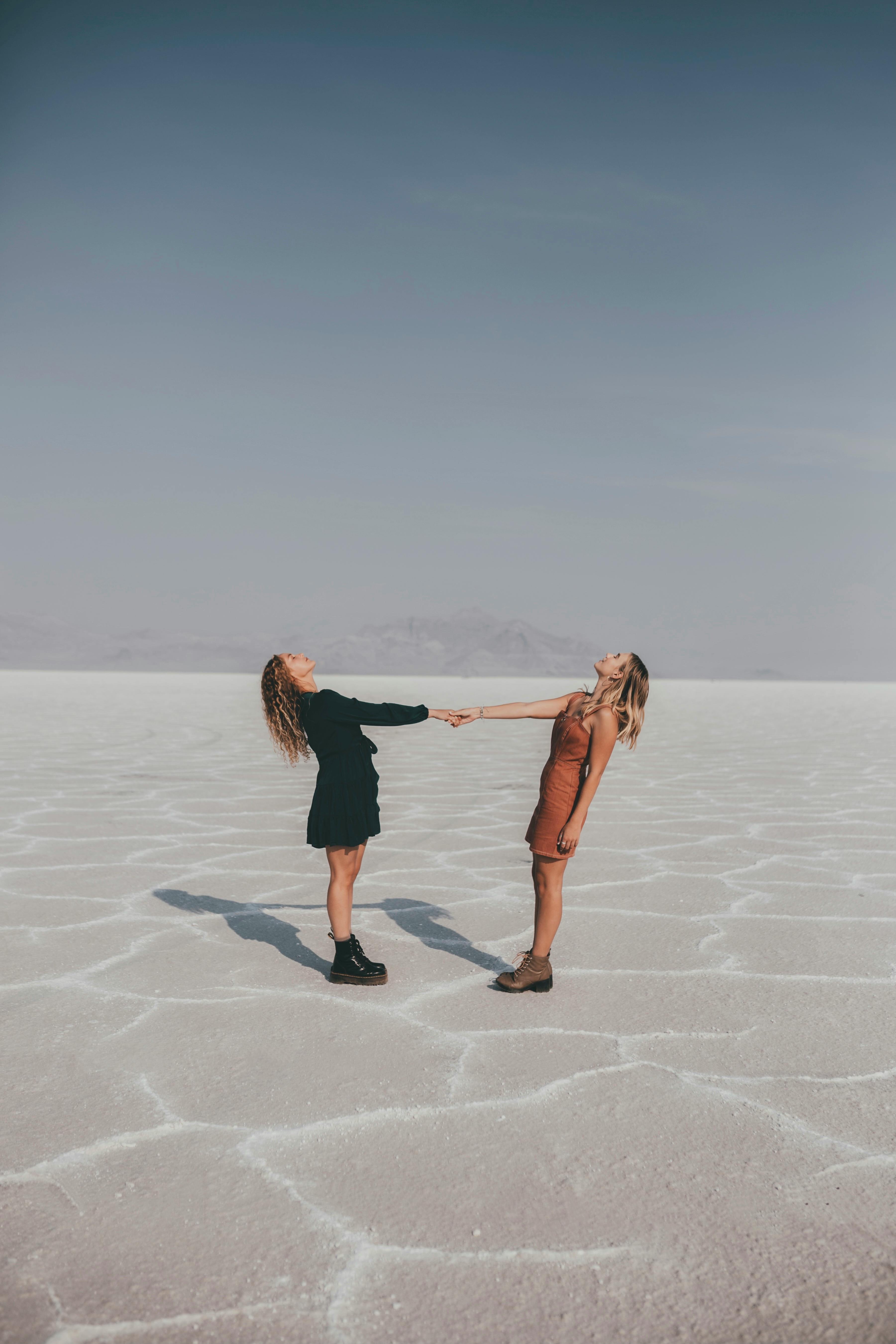 Two women joyfully holding hands on a vast desert landscape, symbolizing friendship and freedom.