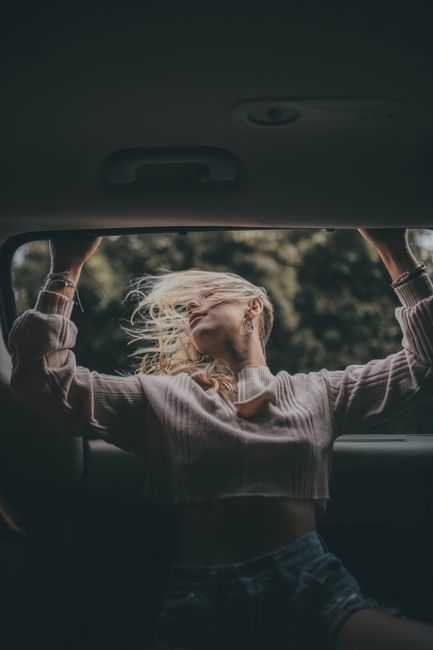 A young woman leans out of a car window, embracing the breeze and natural freedom.