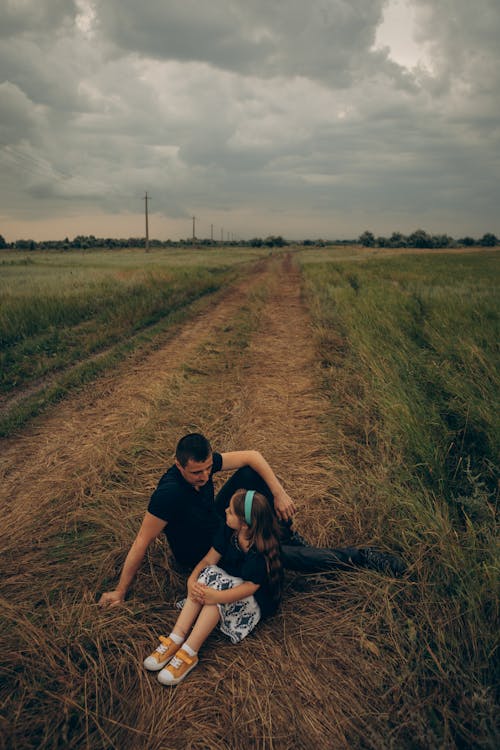 Free Father and Child Sitting on an Unpaved Pathway in the Farmland Stock Photo
