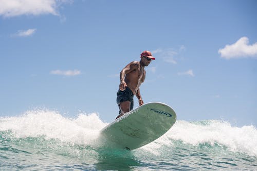 Man Wearing a Red Cap while Surfing at the Beach