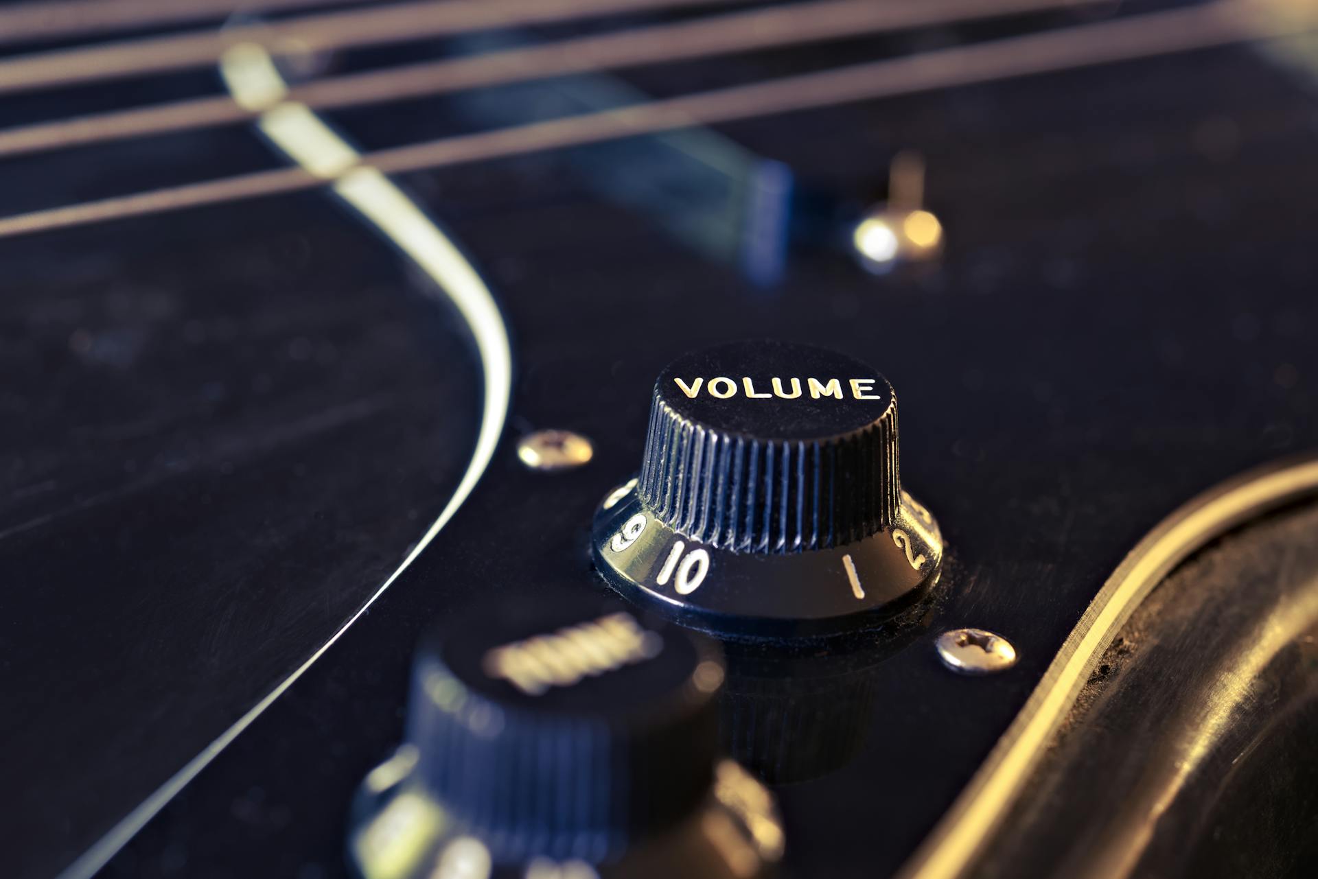 Detailed view of an electric guitar's volume knob with strings in the background.