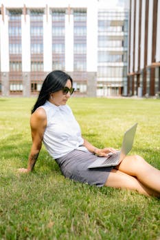 Businesswoman sitting on grass with laptop enjoying outdoor work environment.