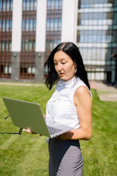 Asian businesswoman standing outside reviewing laptop content with a professional look.