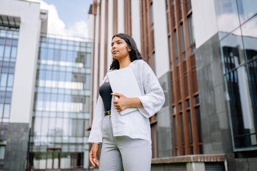Indian professional holding a laptop outside a modern building