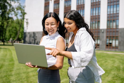Two women happily collaborate on a laptop outside an office building.