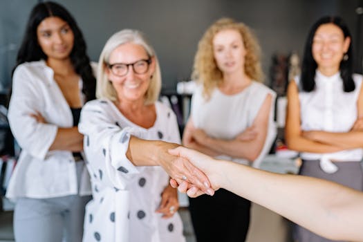 Group of diverse businesswomen confidently shaking hands and smiling in a modern office setting.