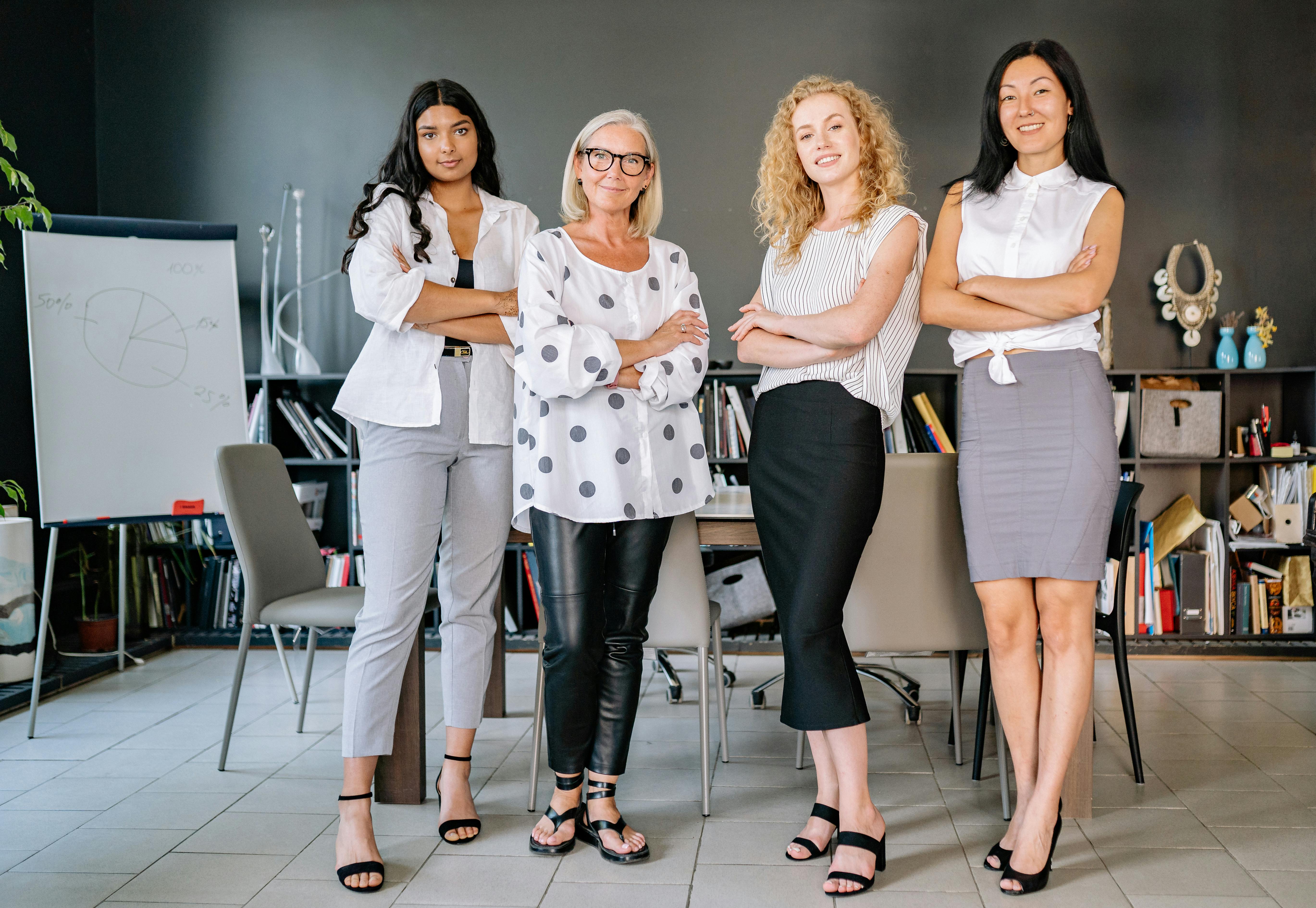 Group of confident businesswomen standing with arms crossed in a modern office setting.