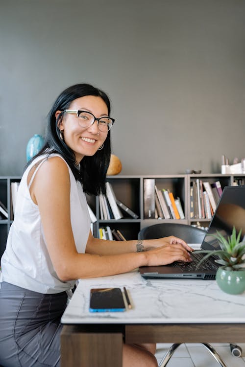 Free Woman Wearing Sunglasses Using a Laptop and Smiling Stock Photo