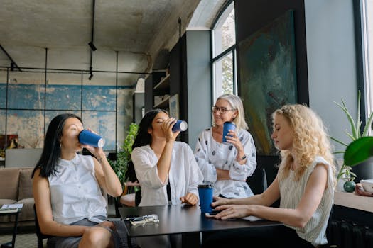 Group of diverse women sharing a coffee break in a modern office setting, fostering teamwork and collaboration.
