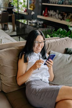 Smiling businesswoman using a smartphone while relaxing on a sofa in an office environment.