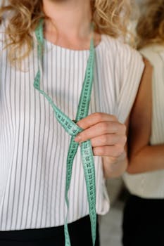 A close-up of a person holding a green tape measure, wearing a striped shirt.