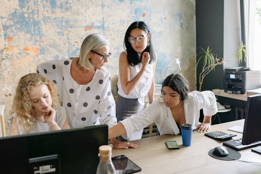 Four women collaborating on a project in a modern office setting, emphasizing teamwork and diversity.