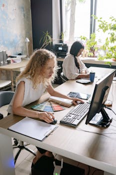 Two women focused on work at a desk, showcasing a vibrant and collaborative office environment.