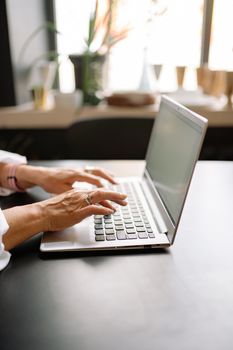 Close-up of a woman's hands typing on a laptop indoors, modern workspace setting.