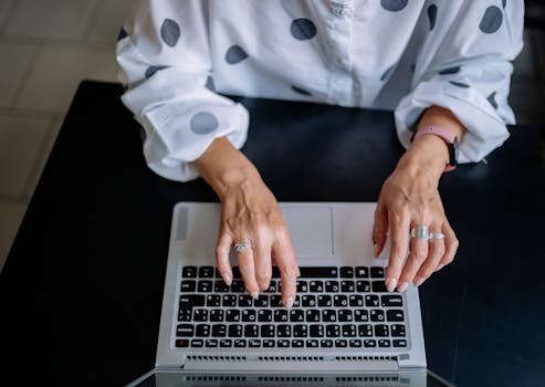 Top view of a woman typing on a laptop, focusing on keyboard and hands with rings.