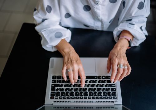 Free Top view of a woman typing on a laptop, focusing on keyboard and hands with rings. Stock Photo