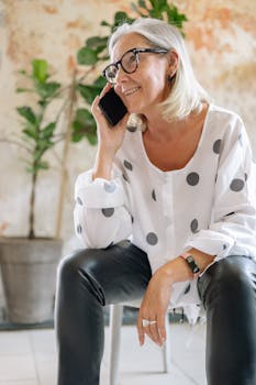 Cheerful senior woman enjoying a phone conversation indoors, smiling warmly.