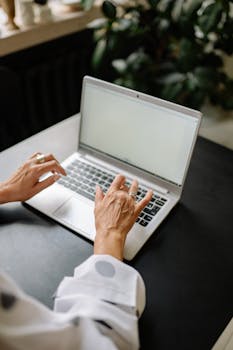 A woman using a laptop at a table indoors, showcasing a minimalist workspace.