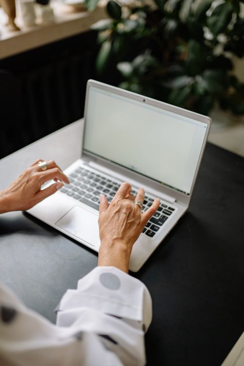 Free A woman using a laptop at a table indoors, showcasing a minimalist workspace. Stock Photo