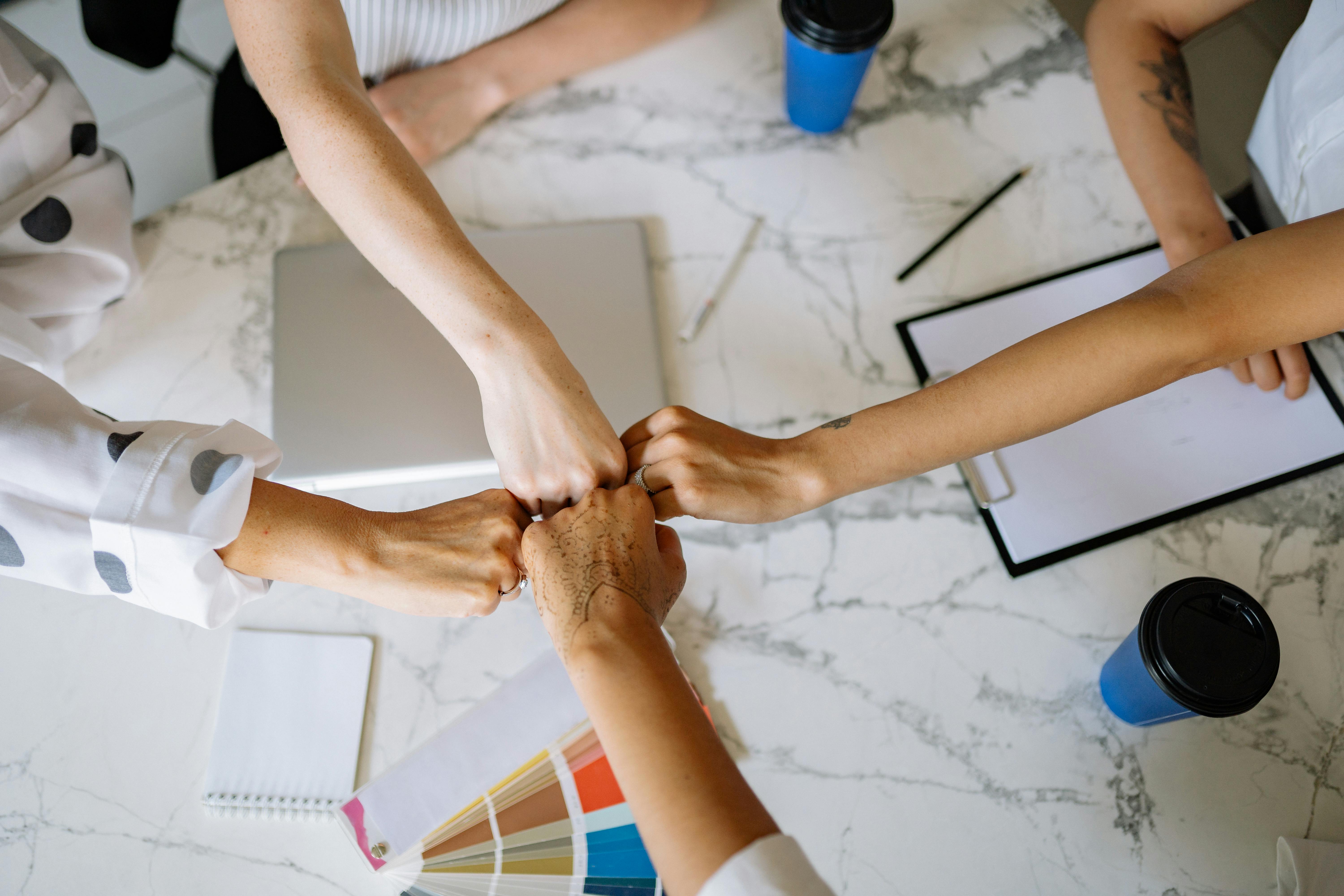 Free Top view of diverse team members fist bumping over a marble table in a collaborative office setting. Stock Photo