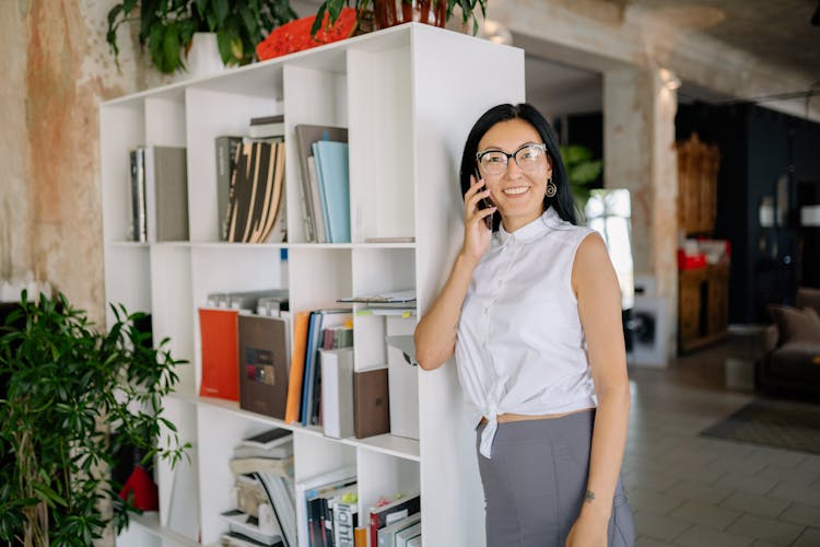 Woman Standing By A Bookcase In An Office And Talking On The Phone 