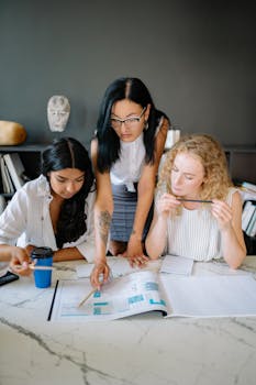 Three women in an office setting discussing a project, highlighting teamwork and diversity.