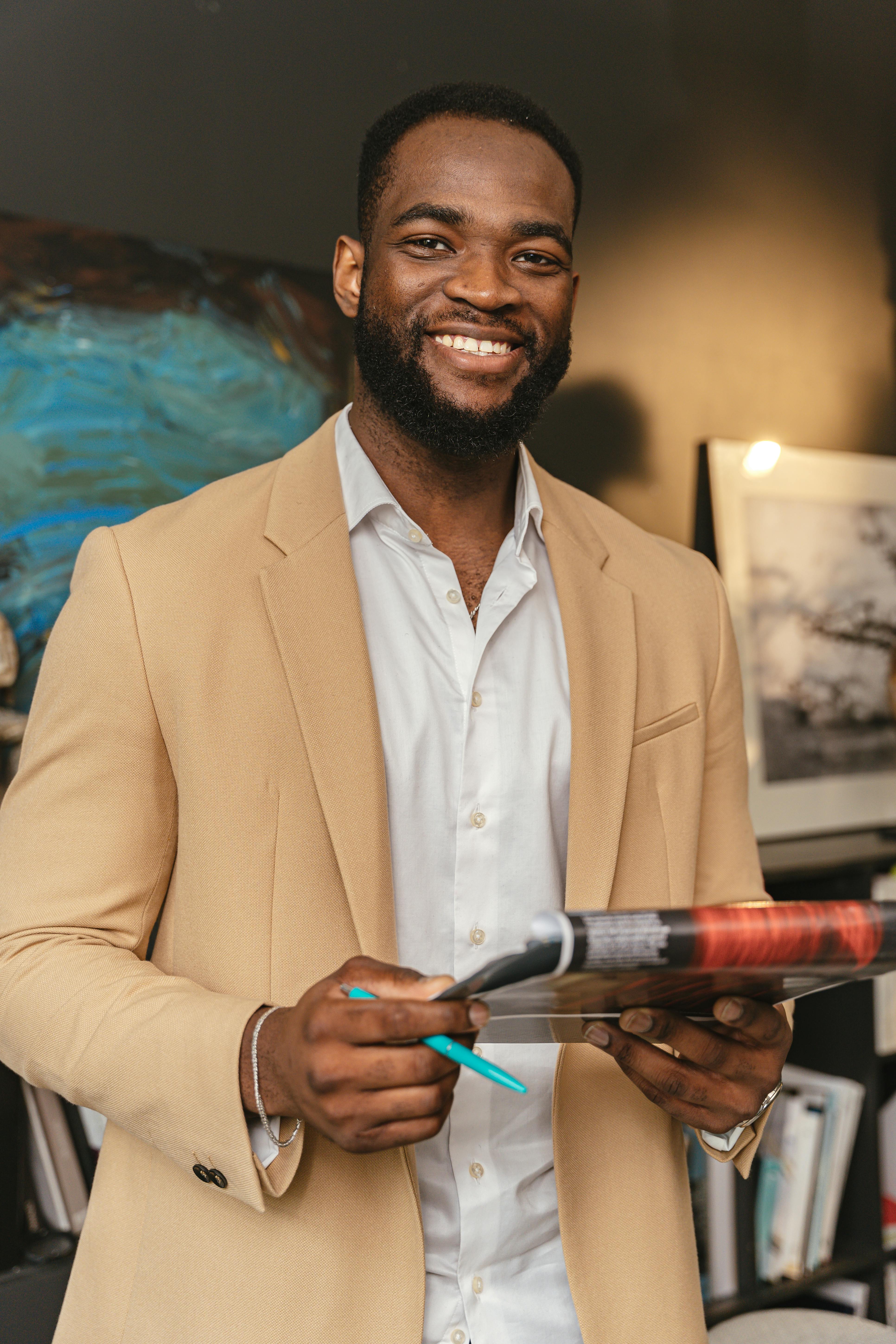 Free Smiling black businessman holding documents in a modern office setting. Stock Photo