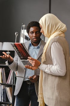 Man and woman in hijab discussing work in modern office. Diverse collaboration with digital tablet.