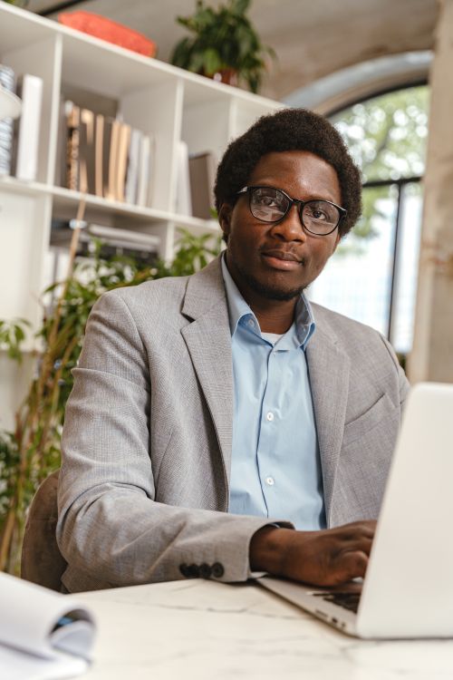 Free Confident professional man in glasses working on a laptop in a modern office setting. Stock Photo