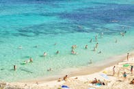 在西班牙马略卡岛的美丽海滩上，人们正享受着阳光明媚的一天，碧绿的海水和沙滩令人心旷神怡