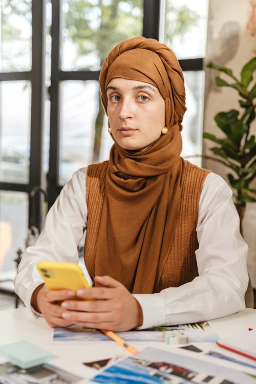 Free Woman in Brown Hijab Holding Yellow Smartphone Stock Photo