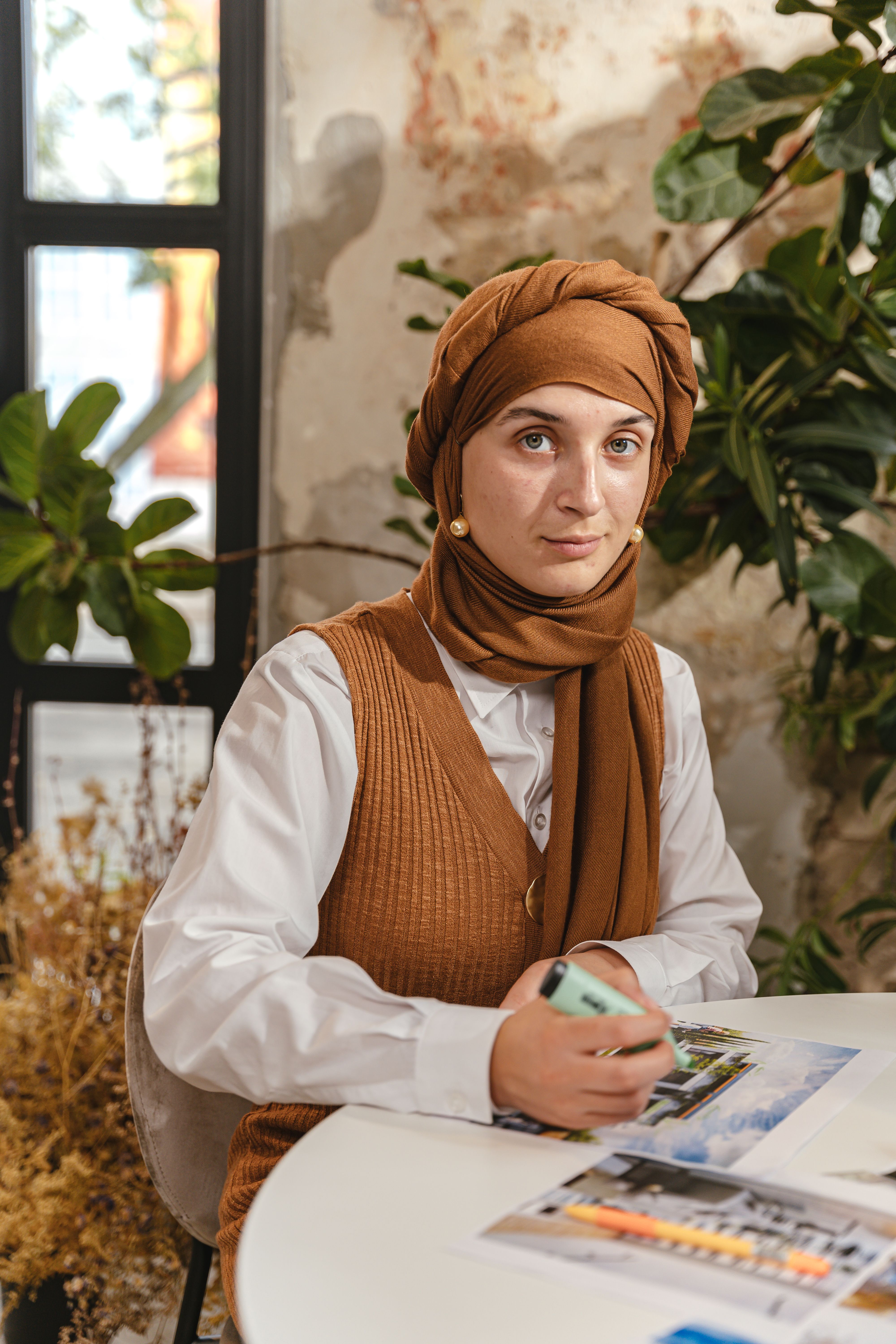 Portrait of a woman in a headscarf working at a desk in an indoor setting with plants.