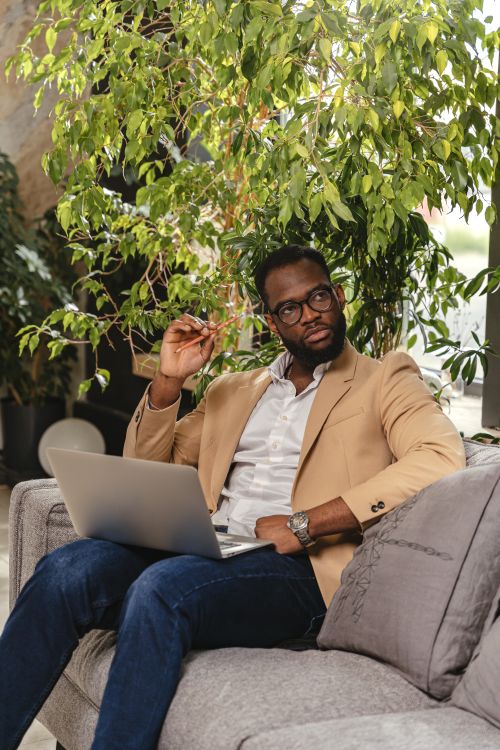 Free African American businessman sitting on a sofa with a laptop, working in a stylish office setting. Stock Photo