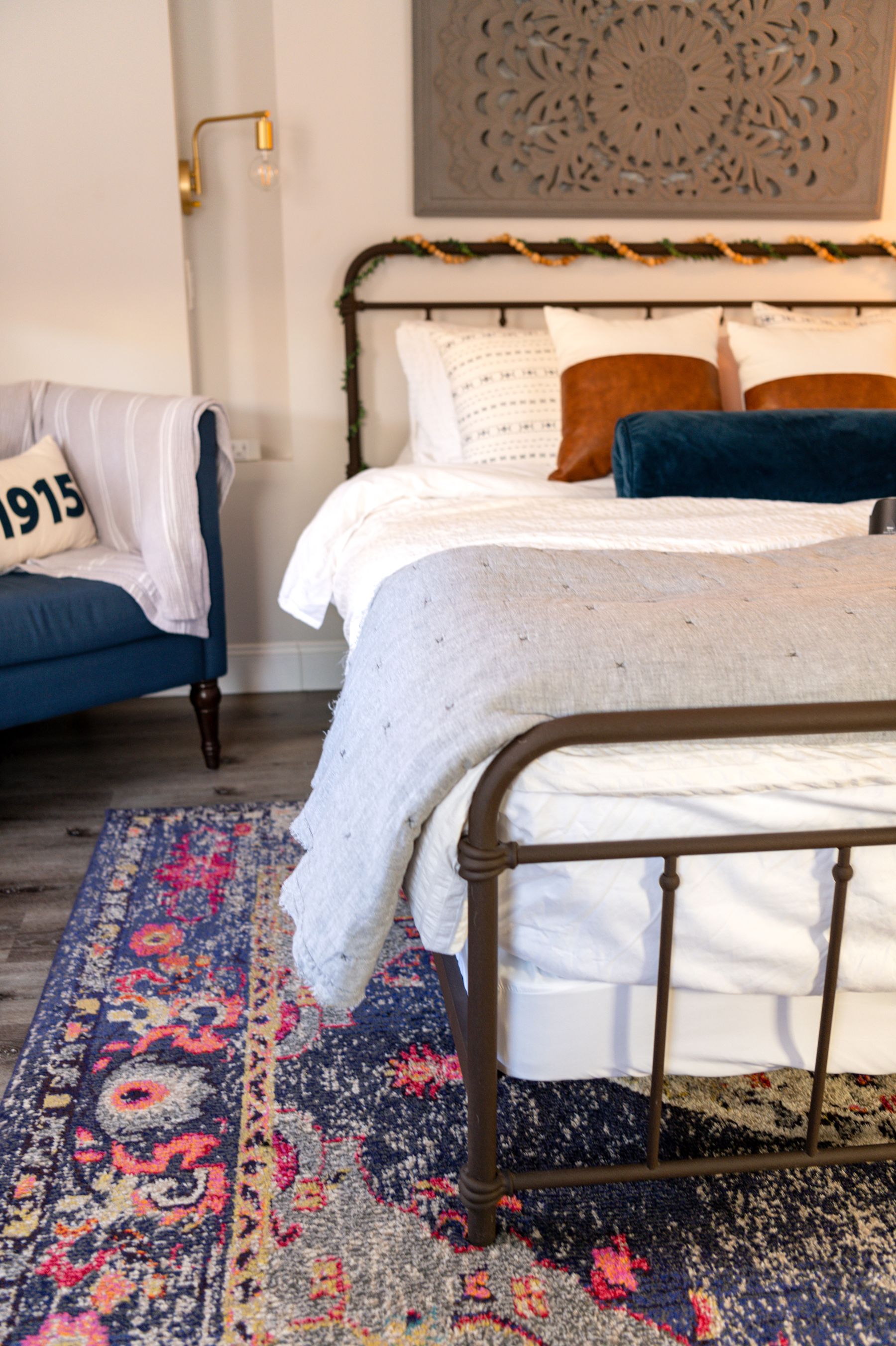 Bohemian bedroom with blue and white bedding, a colorful rug, vintage furniture, plants and framed wall art