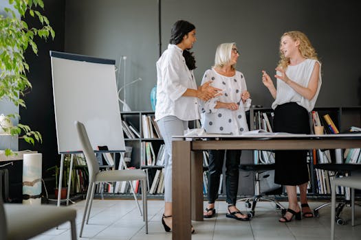 Three diverse women collaborating in a modern office setting, fostering teamwork and creativity.