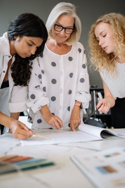 Free Three diverse women actively collaborating on a project in a modern office setting, emphasizing teamwork. Stock Photo