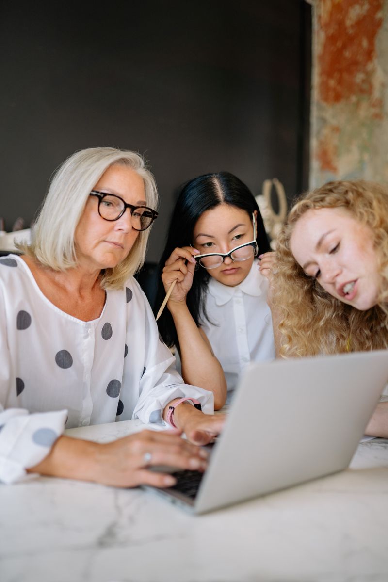 Three diverse women collaborating on a laptop indoors, showcasing teamwork and focus.