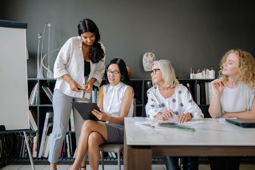 Free Four women collaborating in a contemporary office setting, focusing on teamwork and diversity. Stock Photo